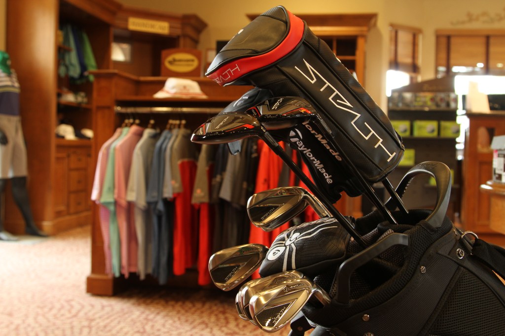 A bag of clubs with a rack of shirts in the background of a proshop 