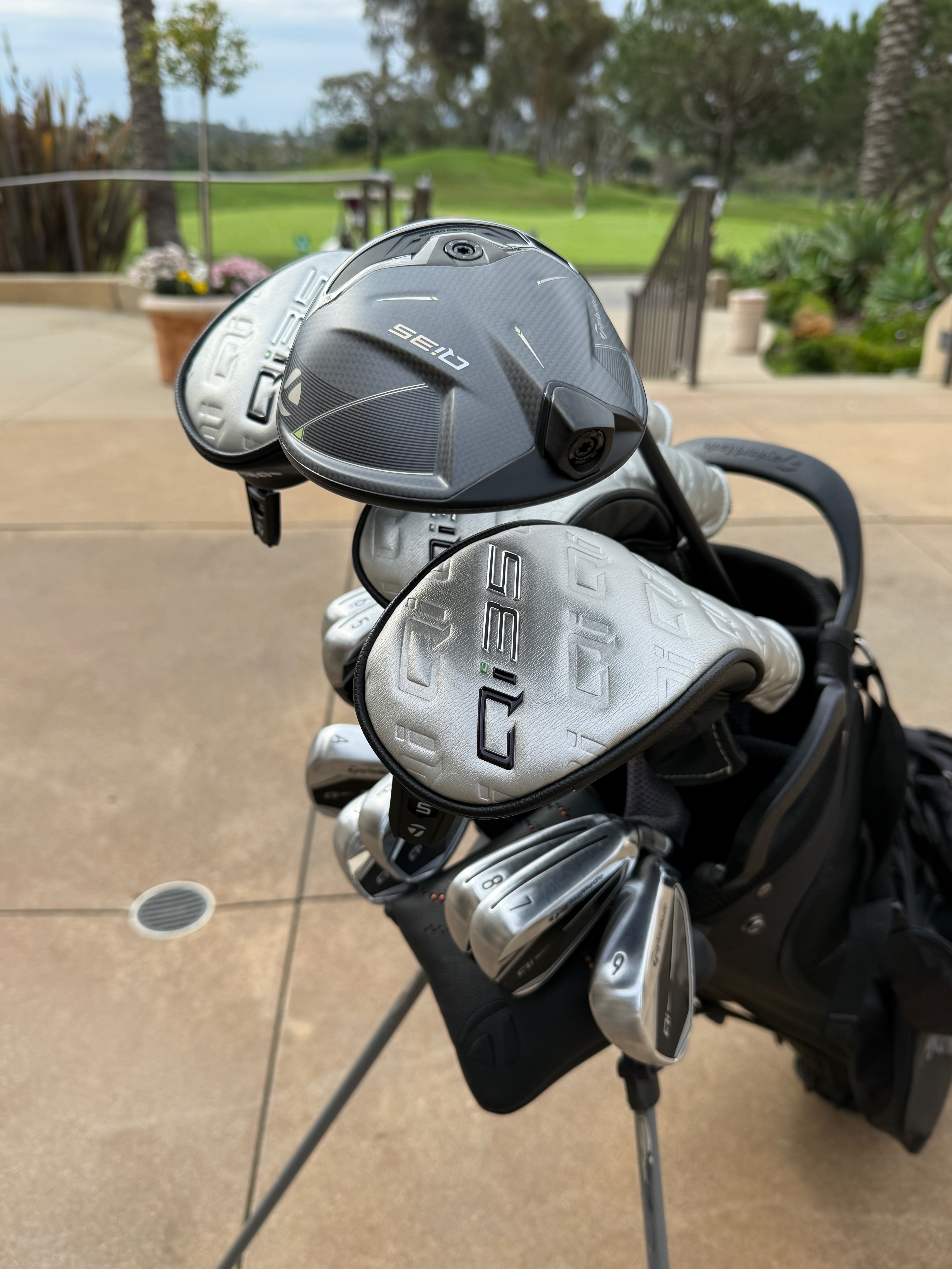 A bag of clubs with a rack of shirts in the background of a proshop 